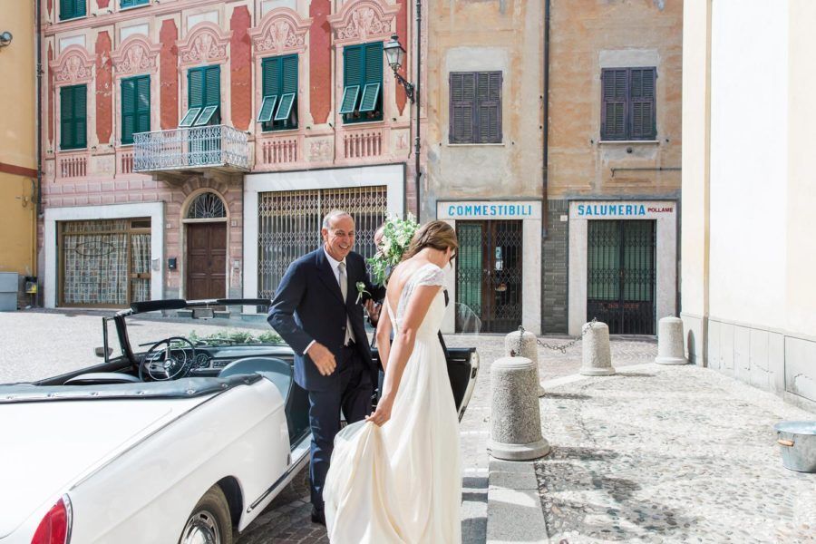 A bride and groom are walking towards a white convertible car.