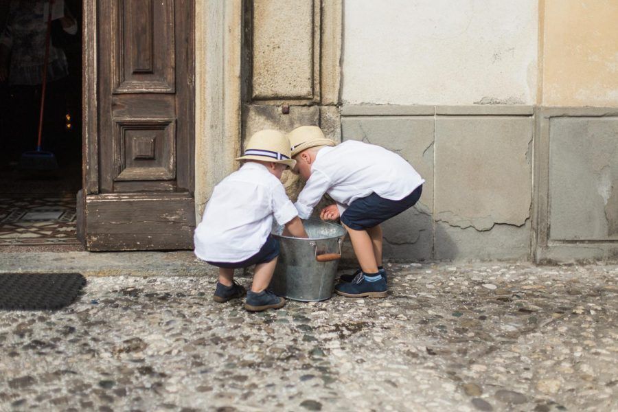Two little boys are playing with a bucket on the sidewalk.