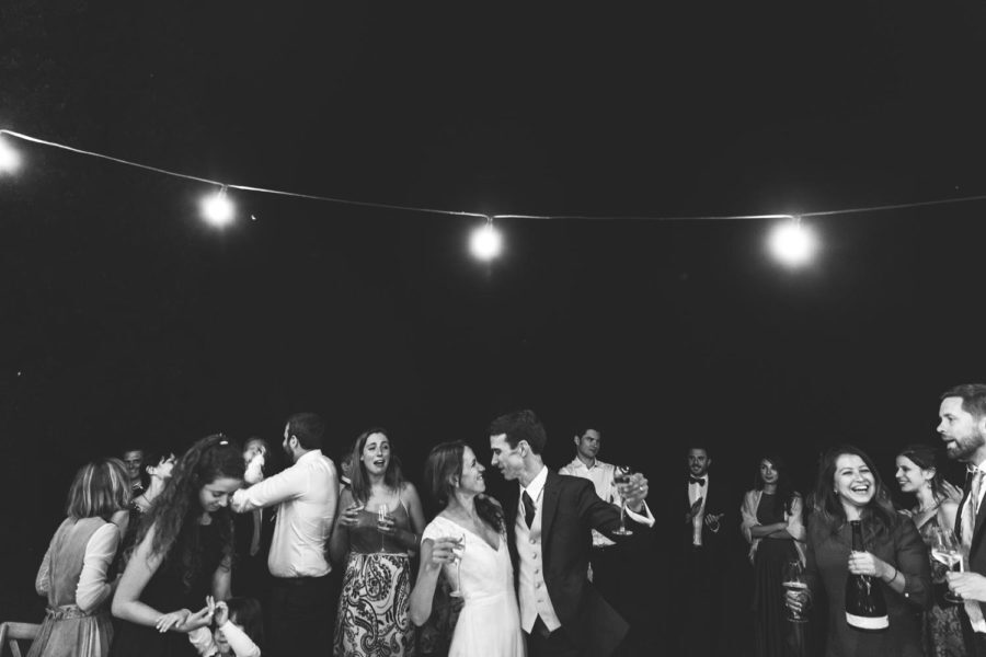 A group of people are dancing under a string of lights at a wedding reception.