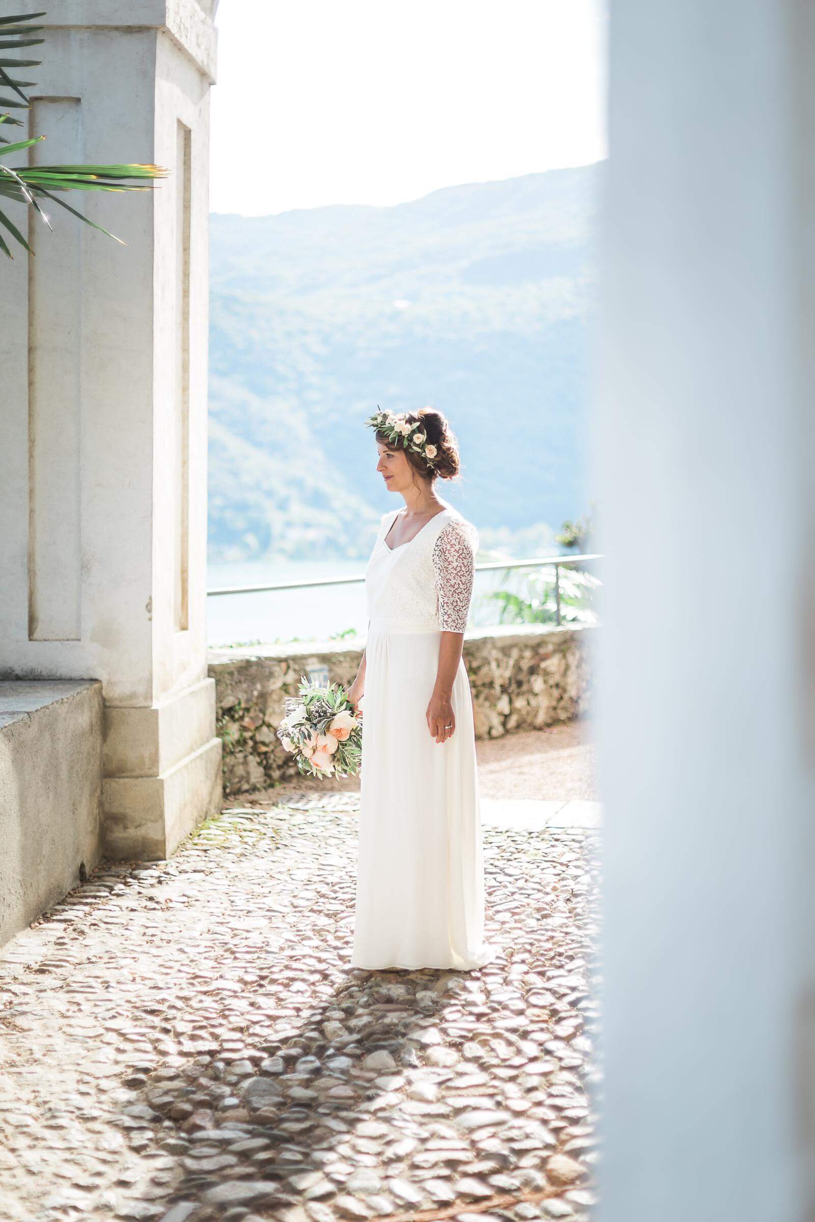 A woman in a white dress and flower crown is standing in front of a building.