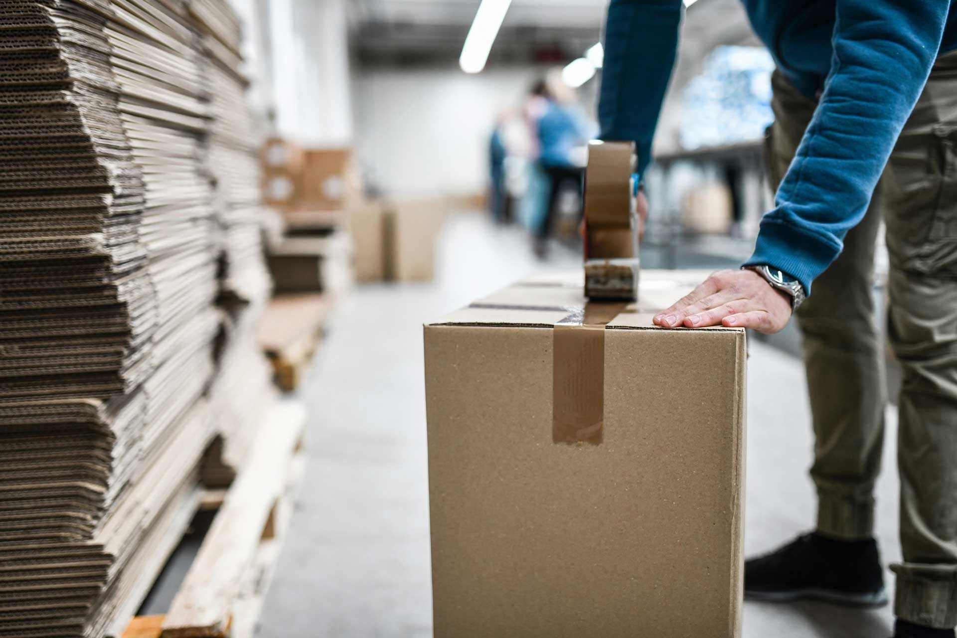 A man is packing a cardboard box in a warehouse.