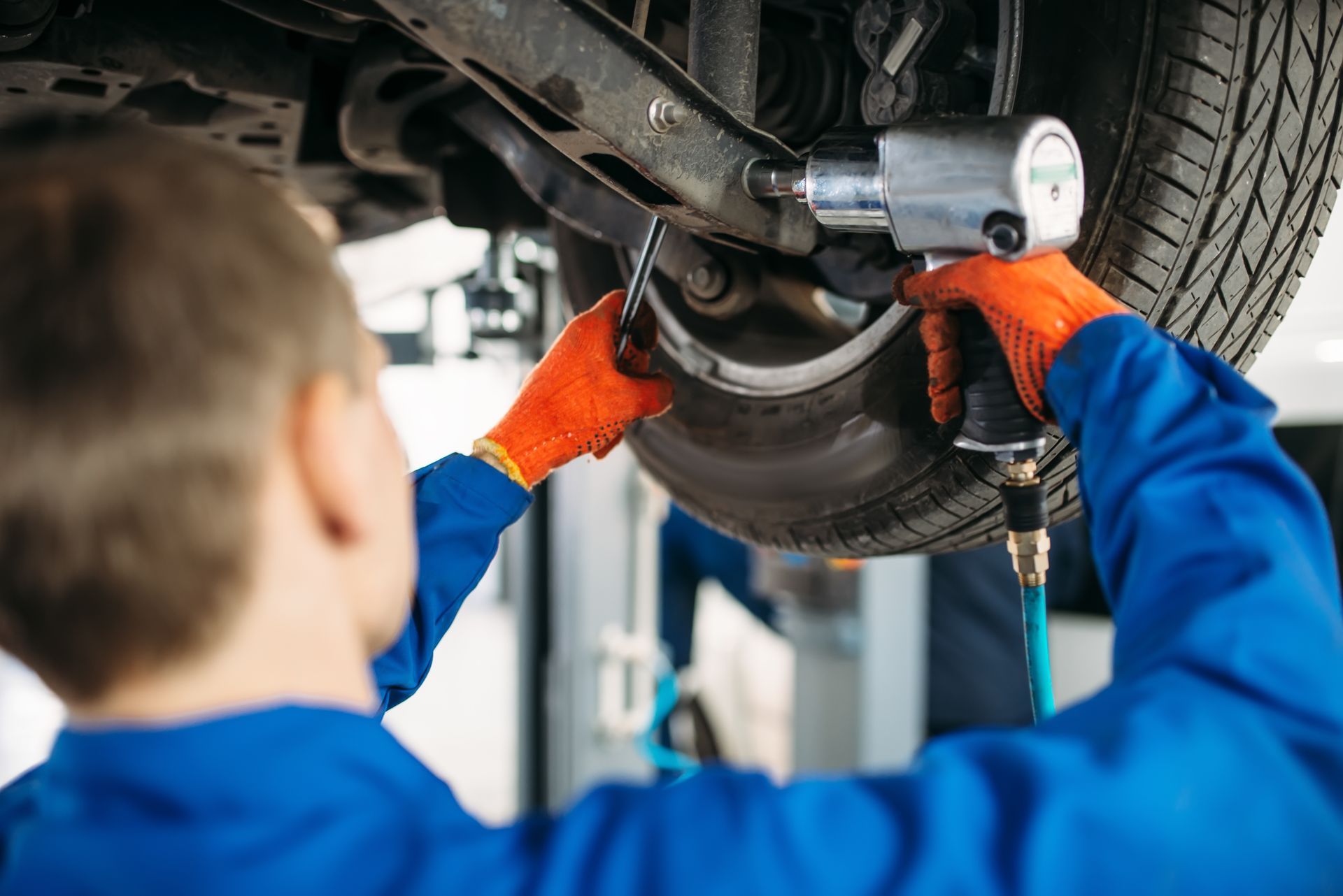 A mechanic is working on the underside of a car.
