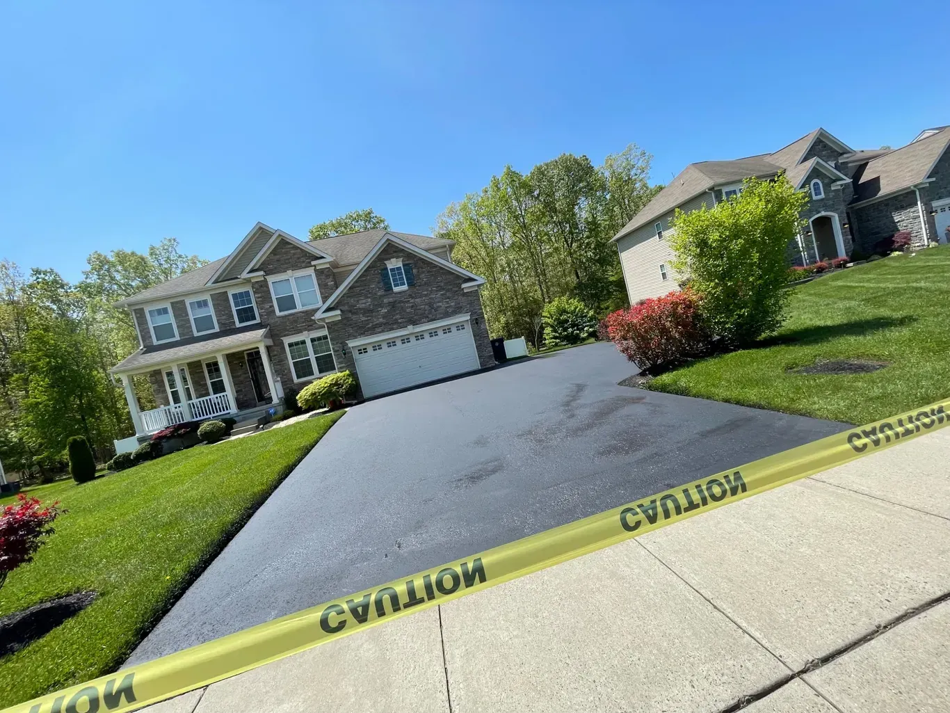 A driveway with a caution tape along the sidewalk in front of a house.