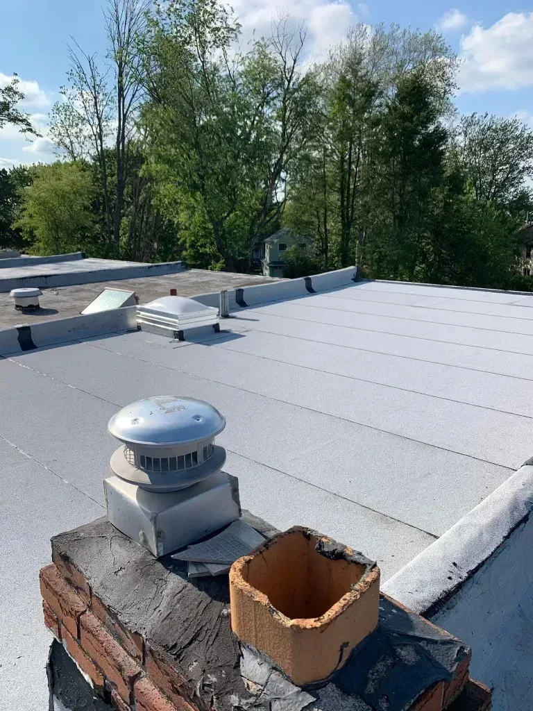 A roof with a chimney on top of it and trees in the background.
