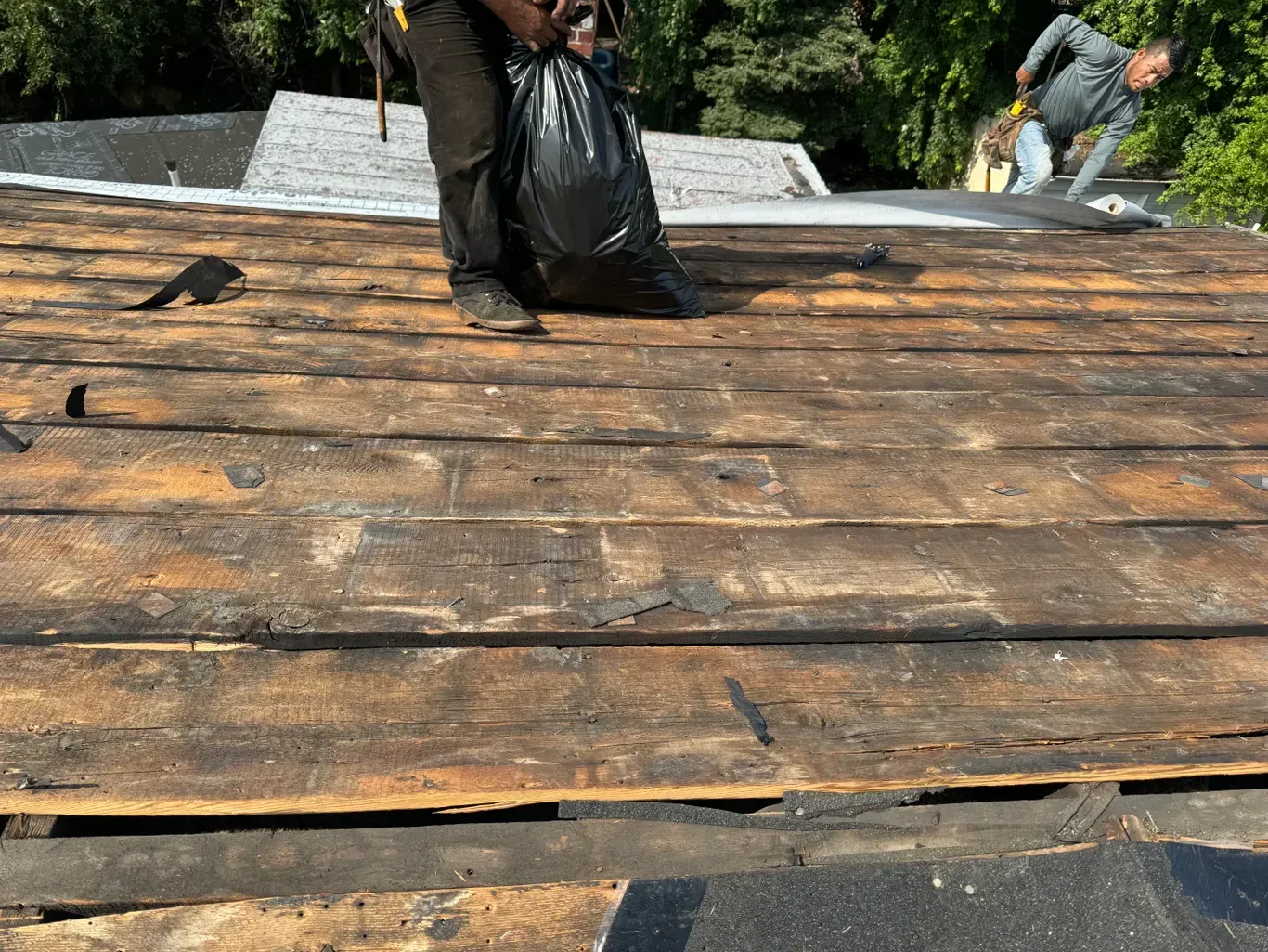 A man is standing on a wooden roof holding a bag of trash.