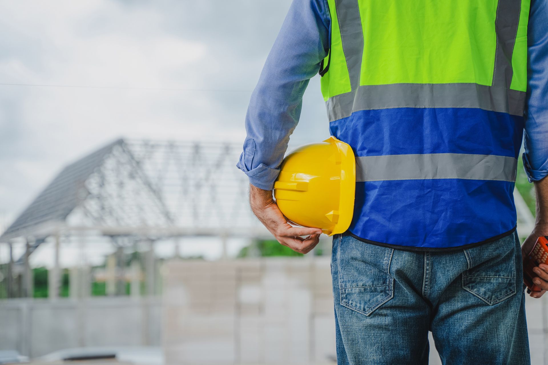 A construction worker is holding a yellow hard hat in his hand.