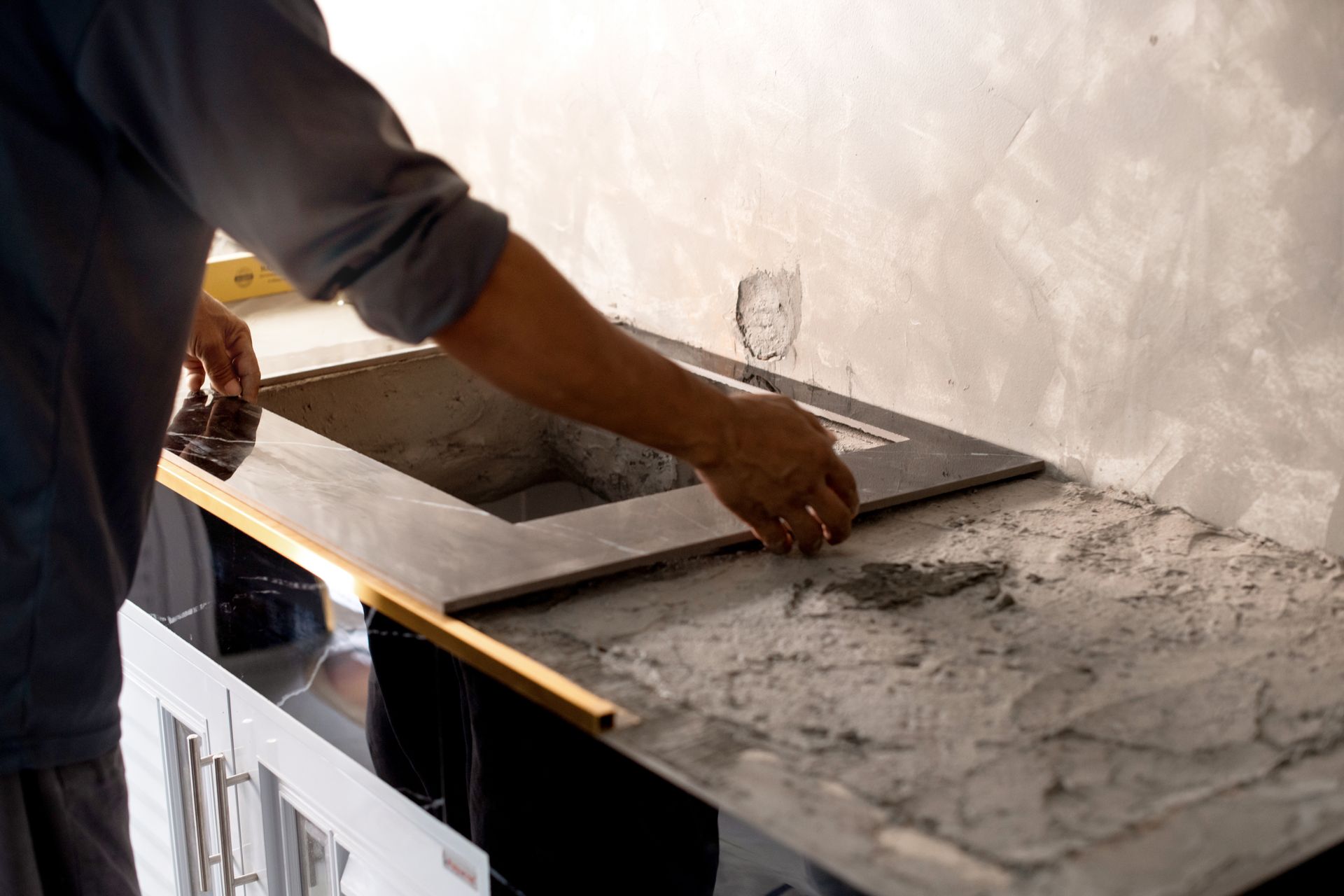 A man is laying tiles on a kitchen counter.