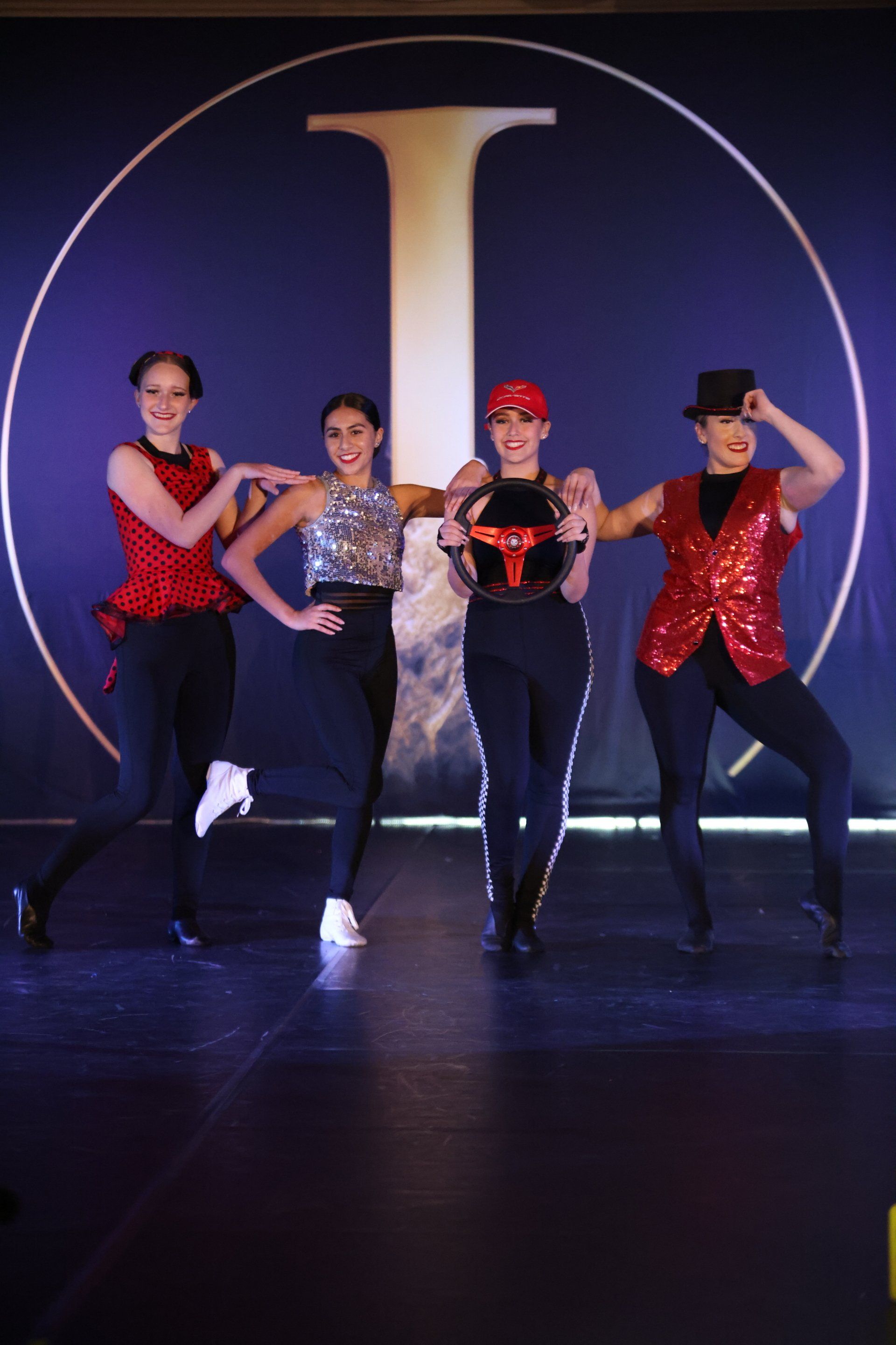 A group of women are dancing on a stage in front of a large letter t.