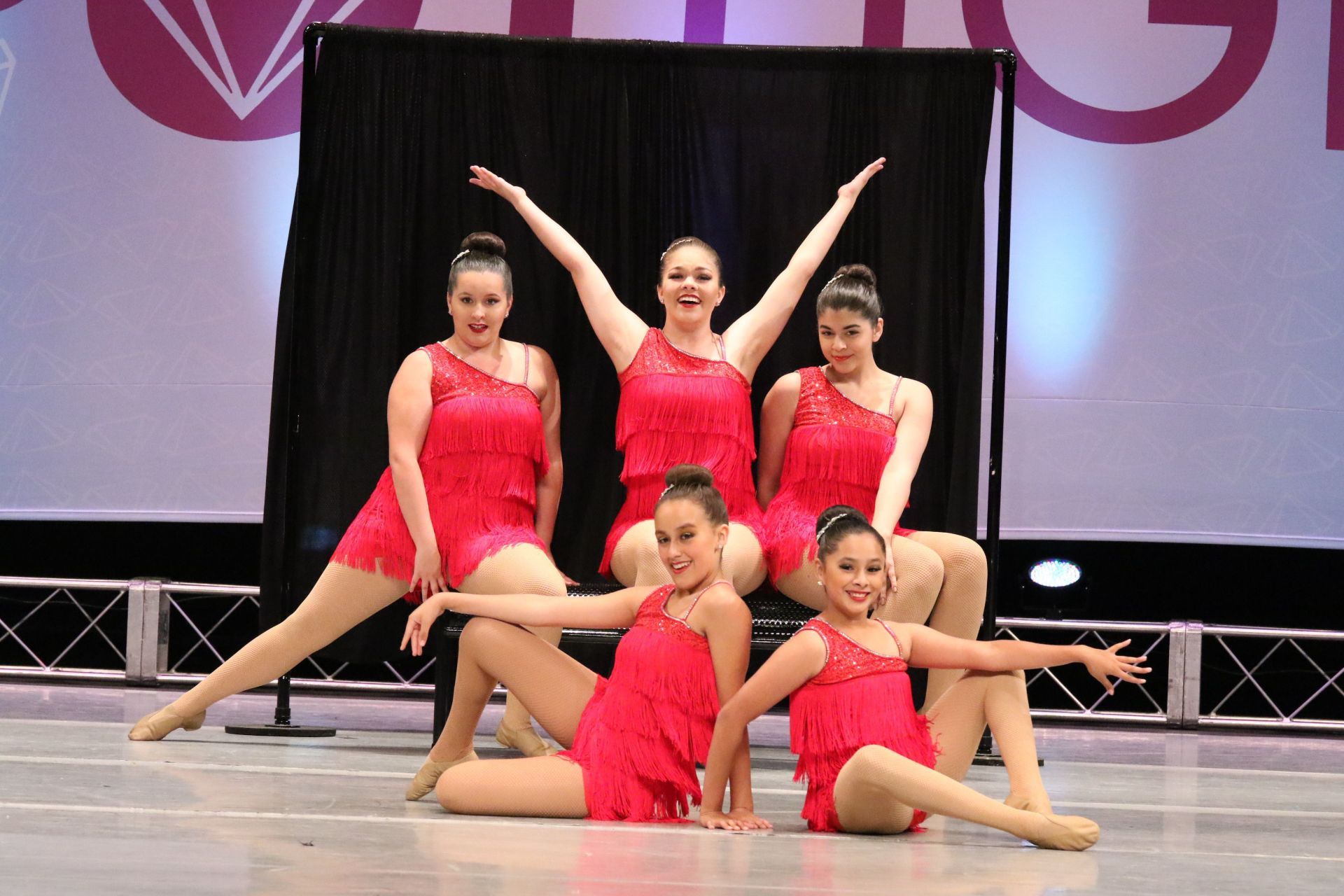 A group of young women in red dresses are posing for a picture on a stage.