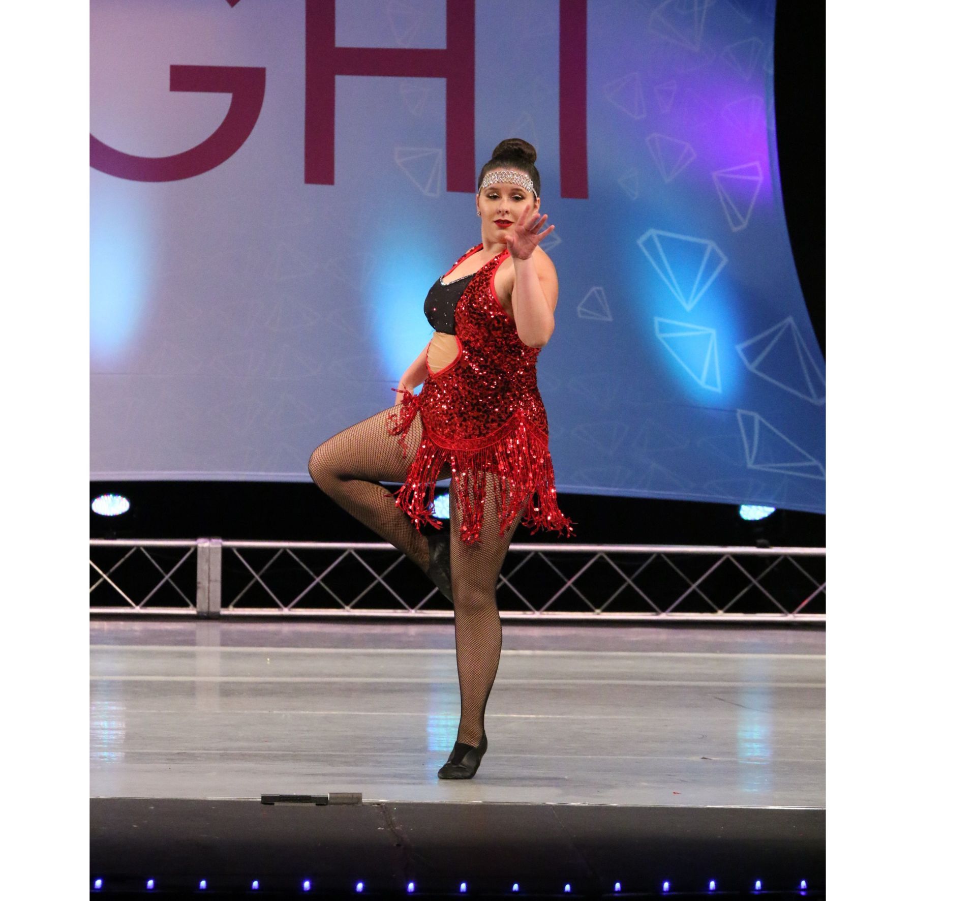 A woman in a red dress is dancing on a stage in front of a sign that says ght