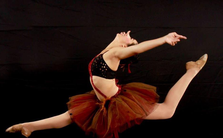 A ballerina in a red tutu is jumping in the air