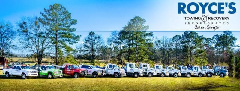Royce's Towing & Recovery trucks parked in a grassy field under a blue sky, with trees in the background.