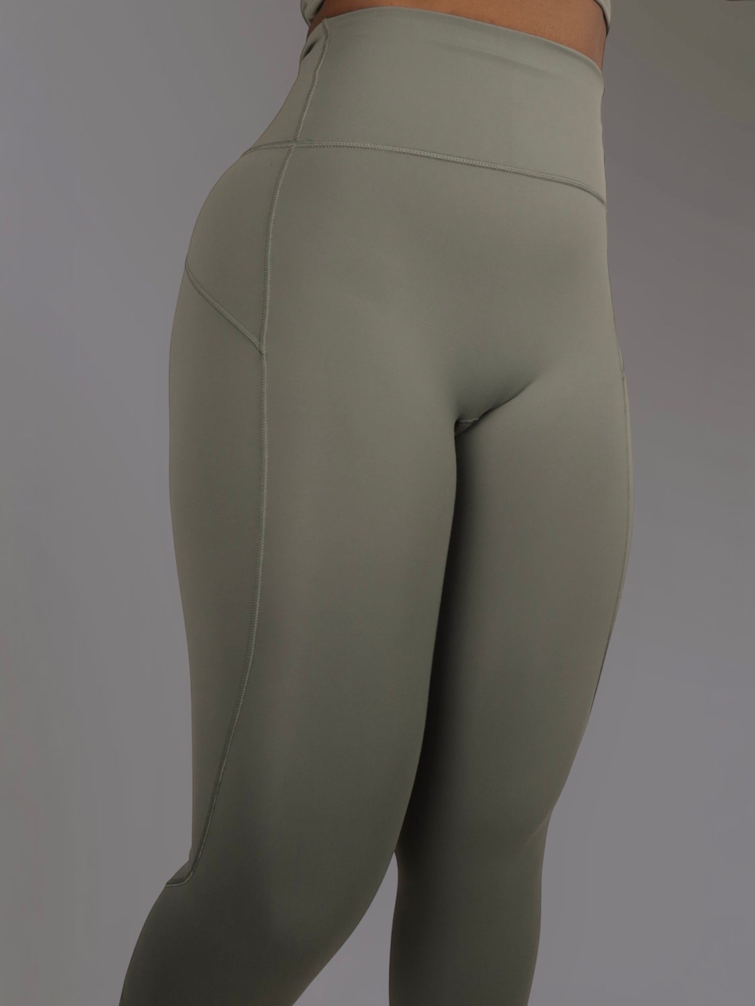 Woman in olive green workout leggings and top, posed against a gray background.