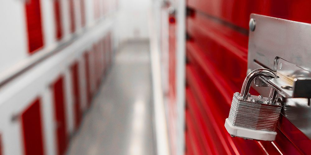 A silver padlock securing a red storage unit door; other units are in the background.