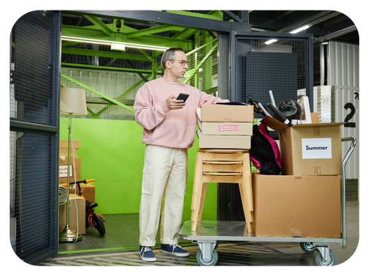 Man with tablet smiling, overseeing couple moving boxes near blue storage unit.