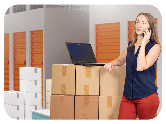 Woman using phone while moving with boxes in the background; phone screen showing a location search.
