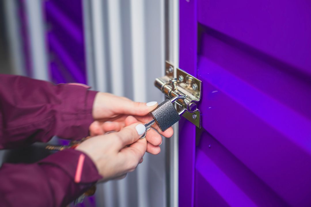 Hands unlocking a purple storage unit door with a key.