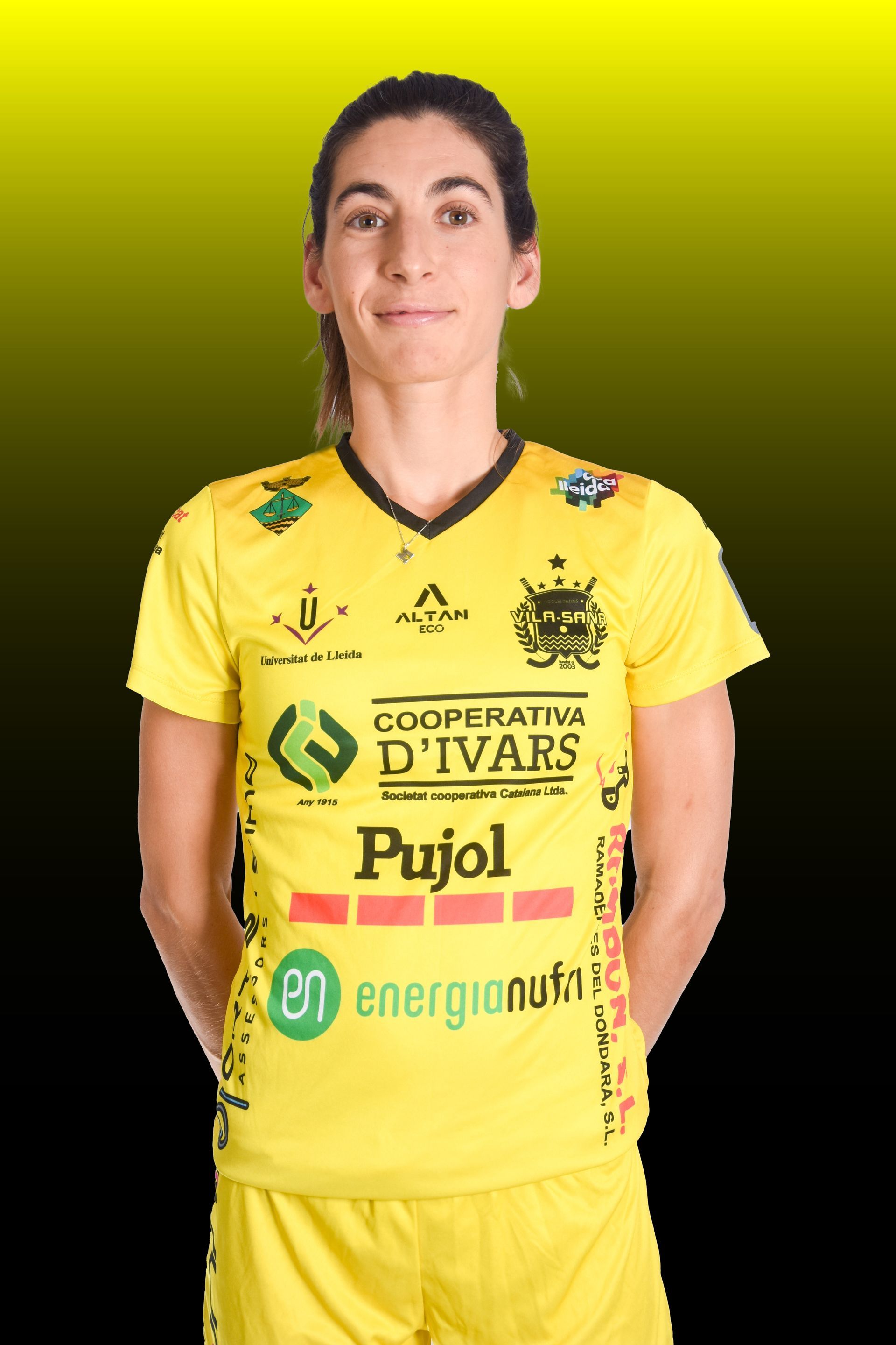 Mujer con camiseta amarilla y cola de caballo, concentrada, en una cancha deportiva.