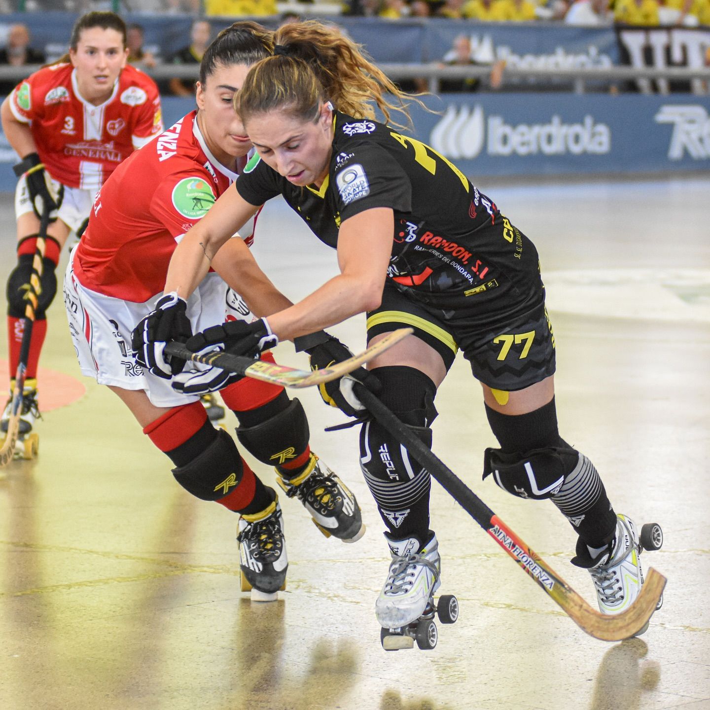 Dos jugadores de hockey sobre patines en acción. Uno de negro y amarillo, otro de rojo, compitiendo por el disco en la cancha.