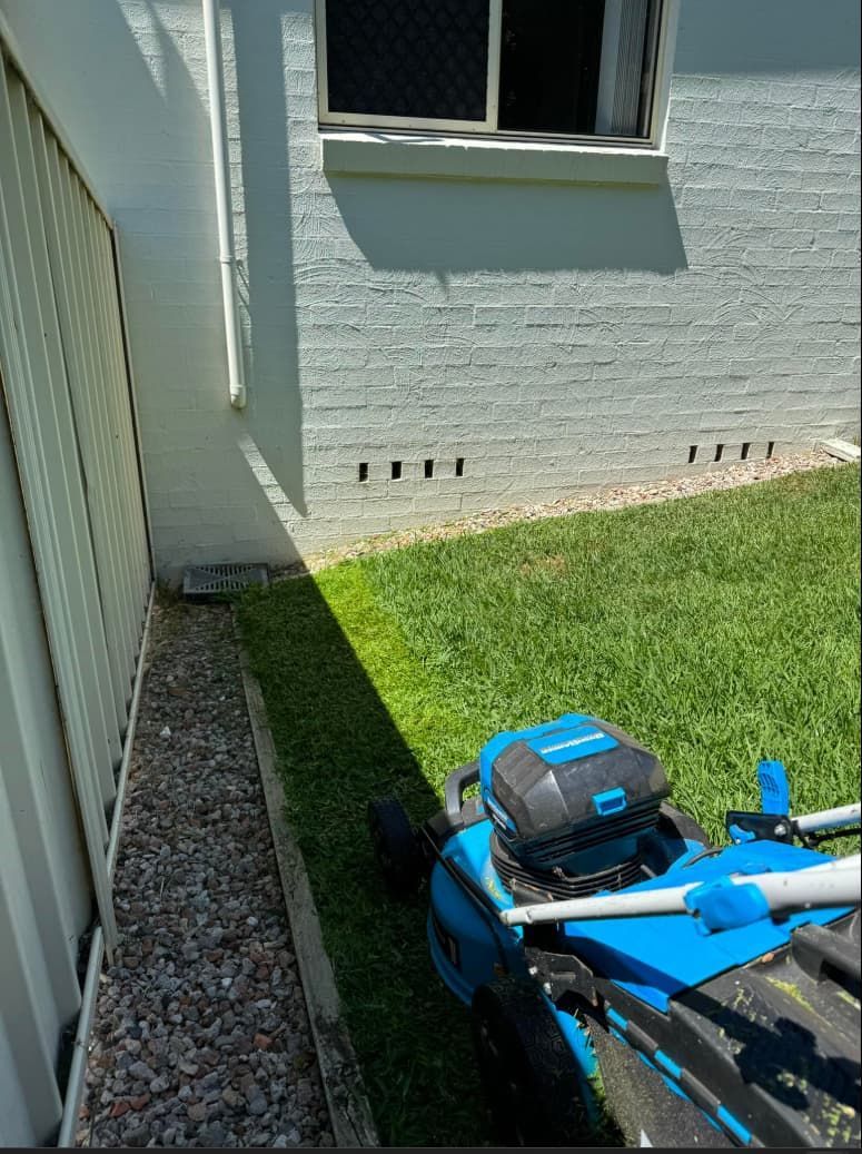 A Blue Lawn Mower Is Parked In Front Of A White Brick Building — Gibbo’s Lawns & Property Maintenance In Salamander Bay, NSW