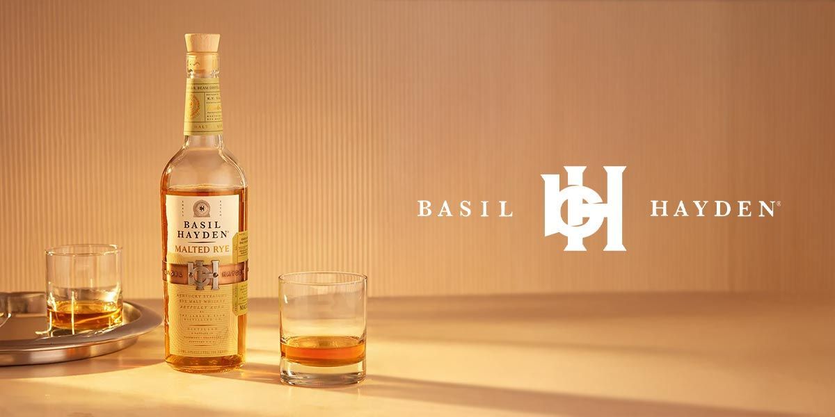 A bottle of basil hayden whiskey and two glasses of whiskey on a table.