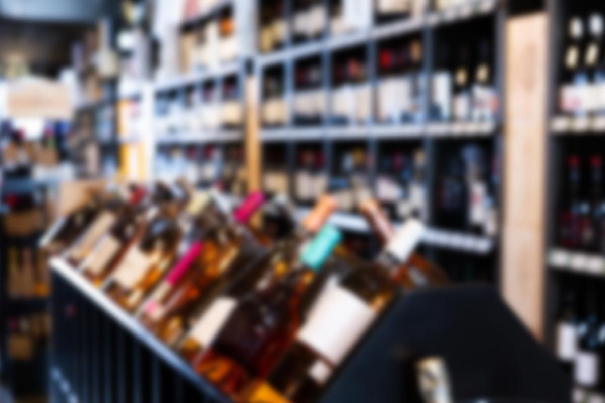 A blurred image of a wine store filled with lots of bottles of wine.