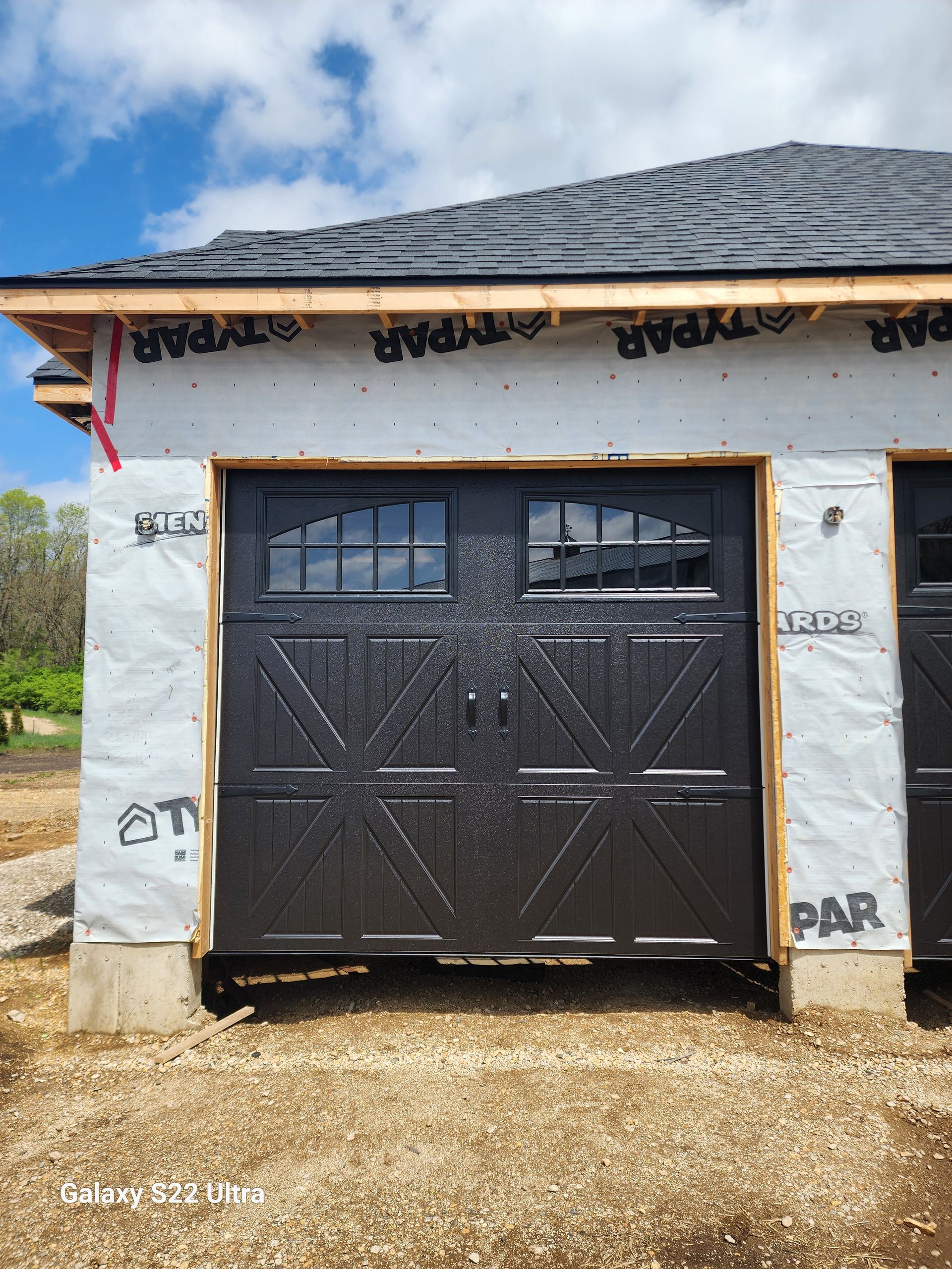 A black garage door is sitting in front of a house under construction.