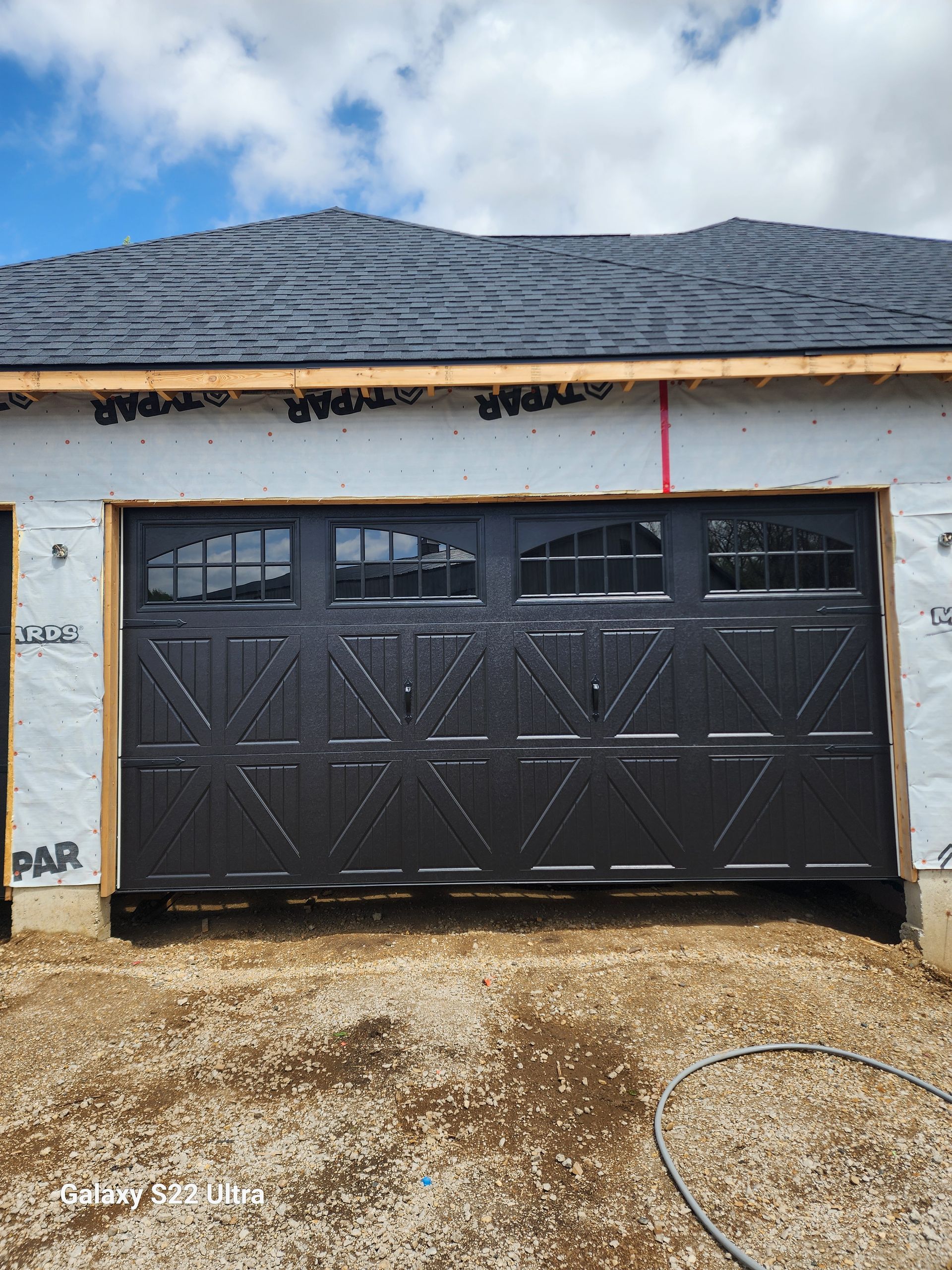 A black garage door is sitting in front of a house under construction.