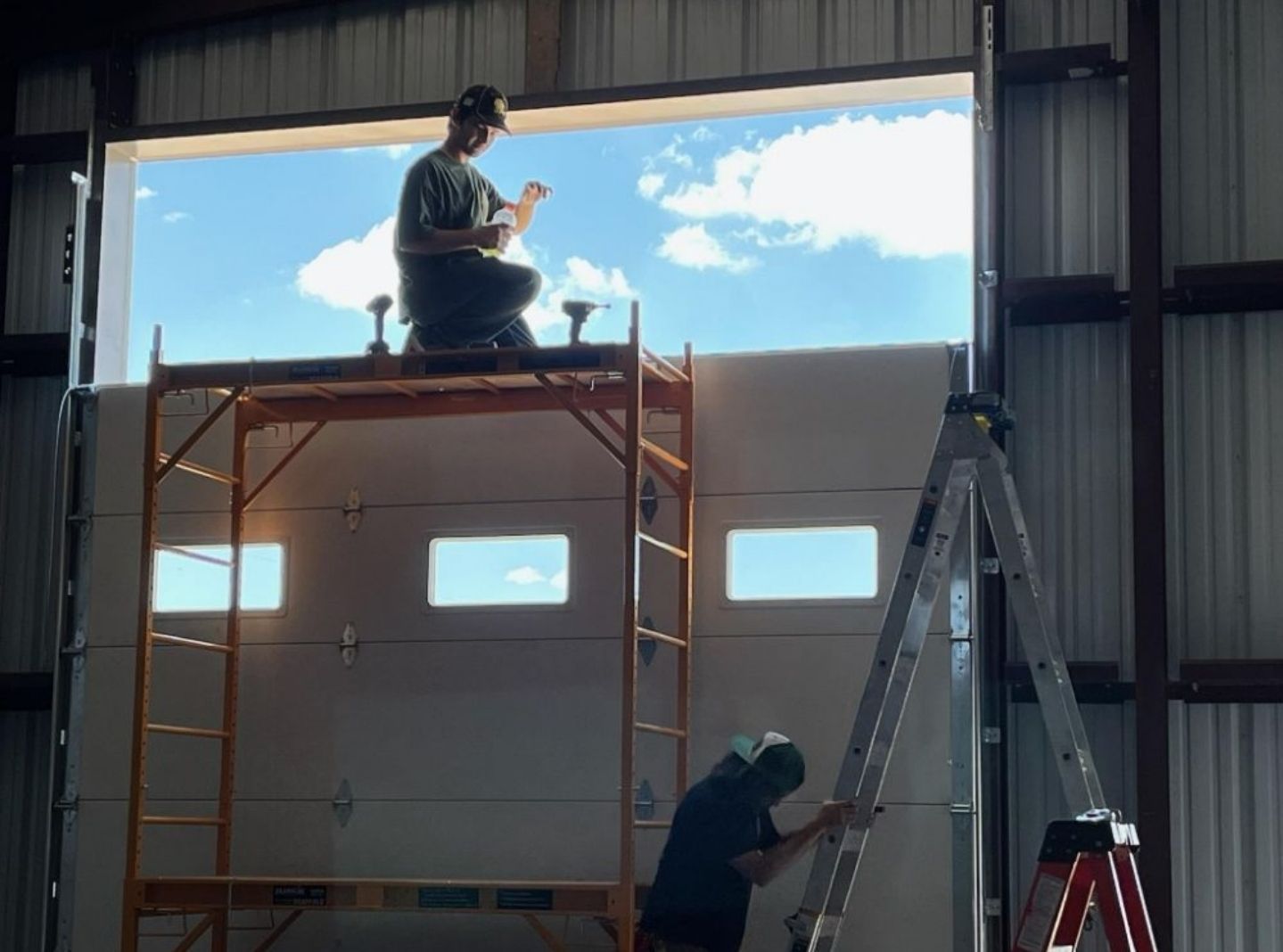 A man sitting on a scaffolding working on a garage door