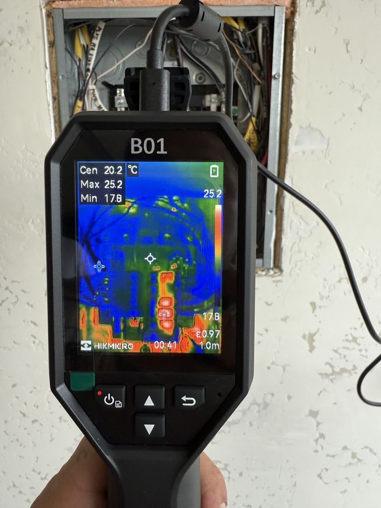 A person is holding a thermal camera in front of a wall.