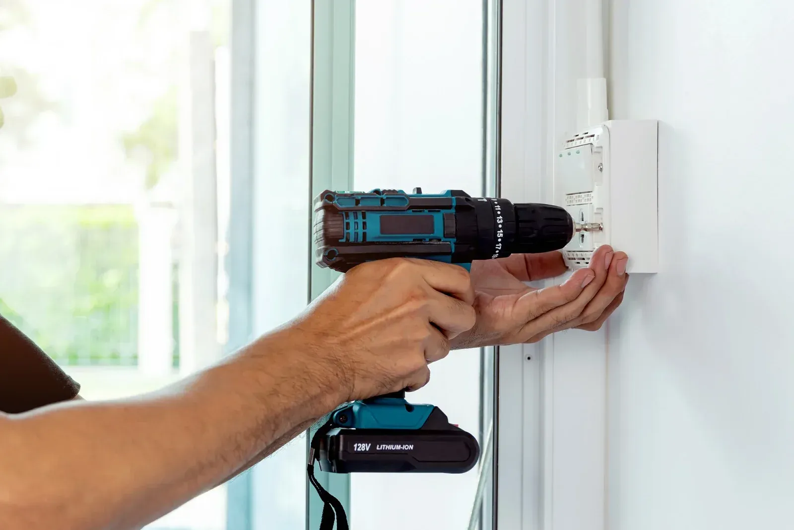 A man is using a drill to install a plug on a wall.