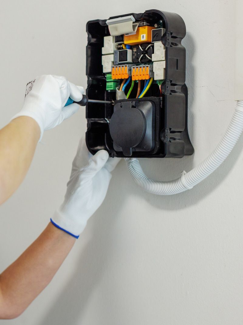 A person is using a screwdriver to fix a box on a wall.