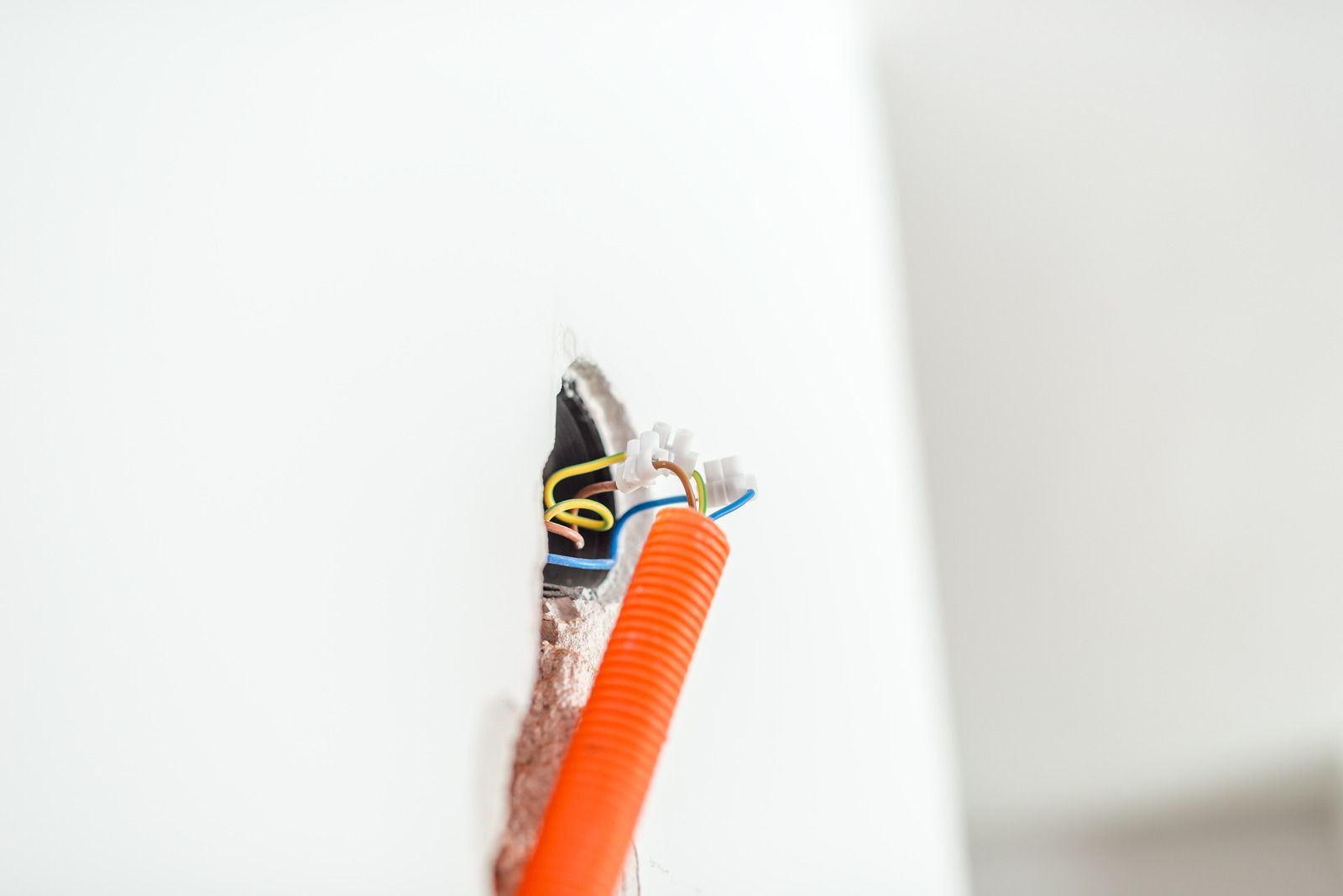 A close up of an orange wire coming out of a hole in a wall.