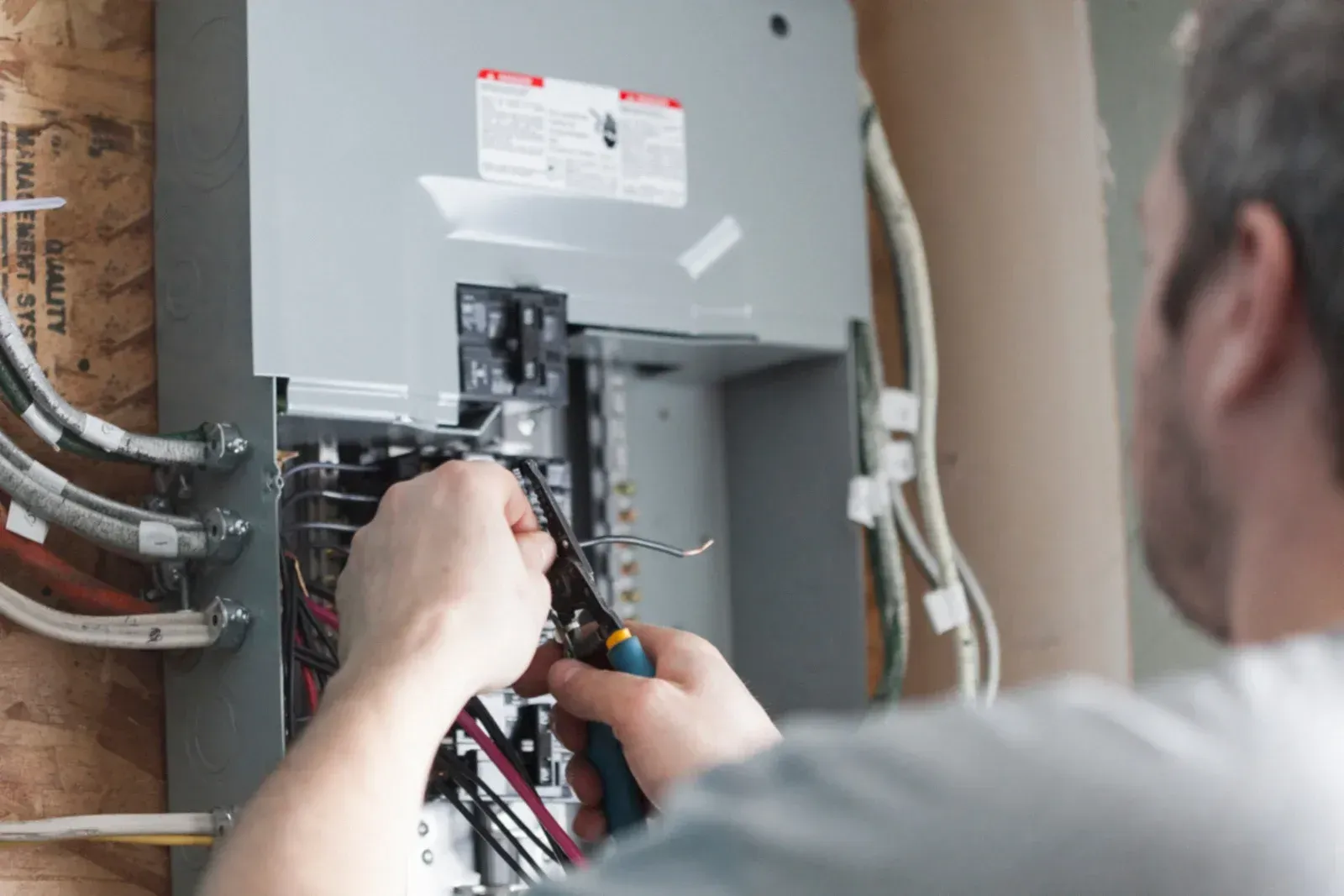 A man is working on an electrical box with a pair of pliers.