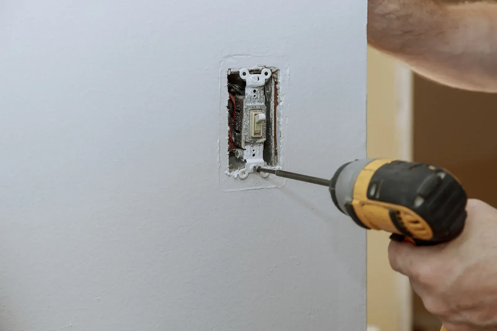 A person is using a drill to install a light switch on a wall.