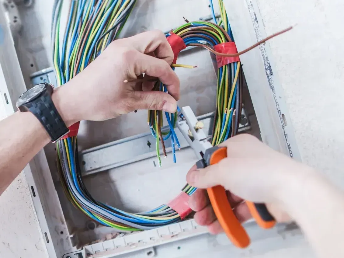 A person is working on an electrical box with a pair of pliers.