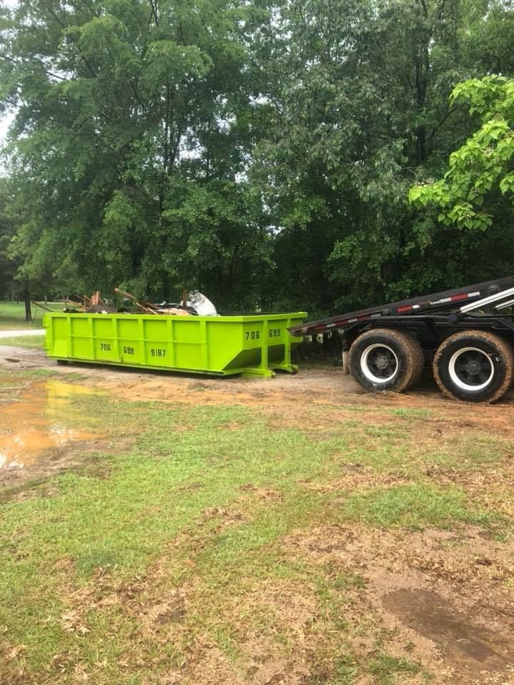 A green dumpster is sitting on top of a trailer in a field.