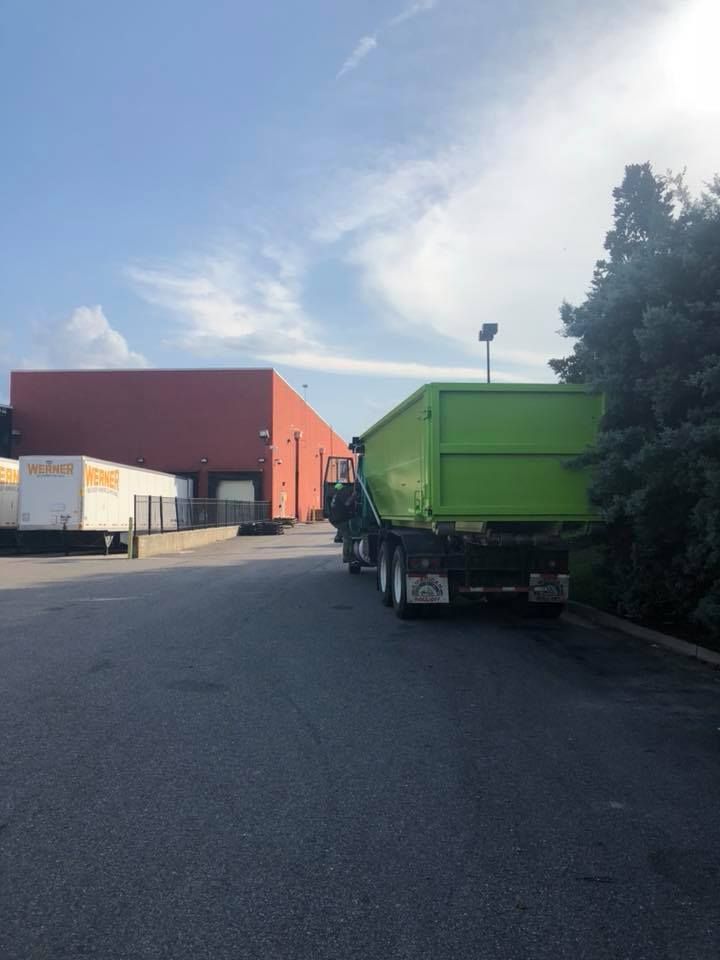 A green dumpster truck is parked in a parking lot in front of a building.