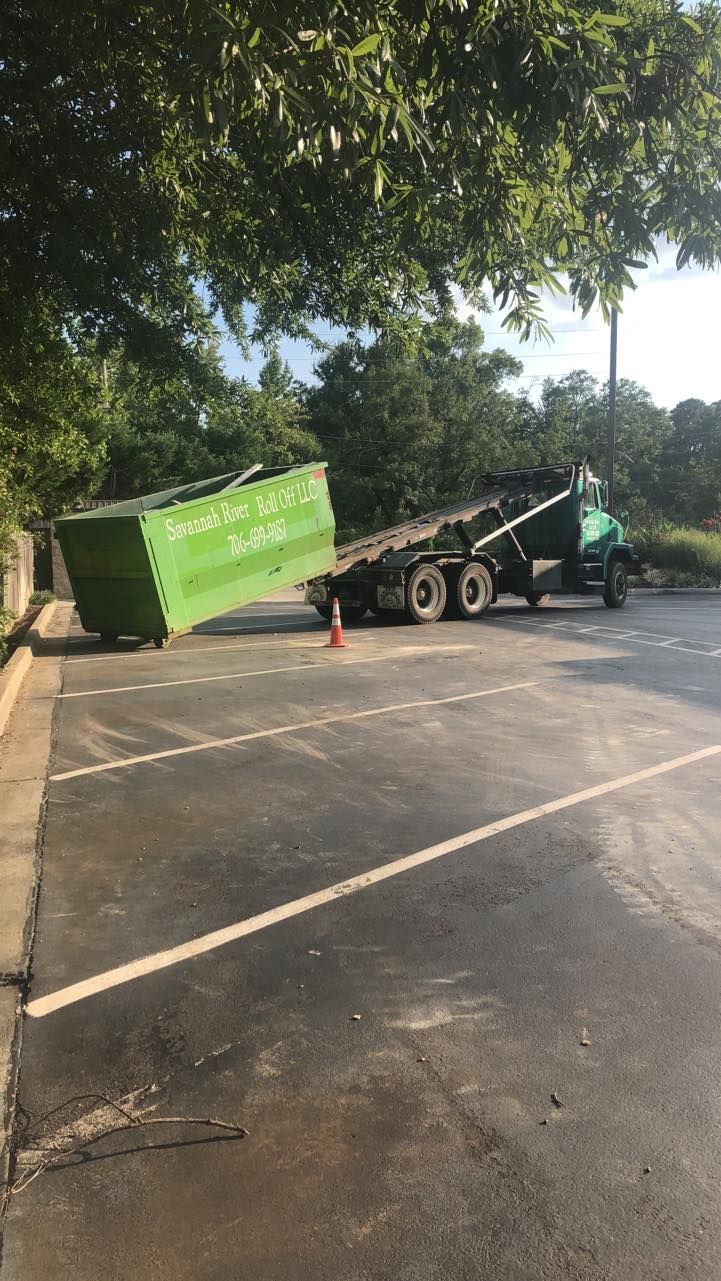 A green dumpster is sitting in a parking lot next to a truck.