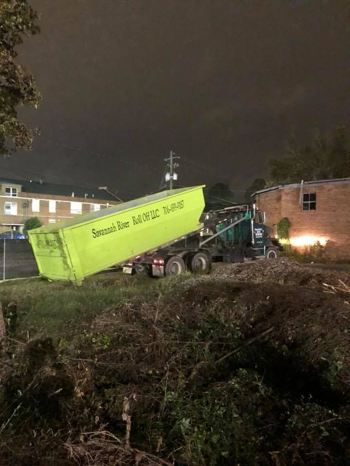 A dumpster is being loaded onto a truck at night.