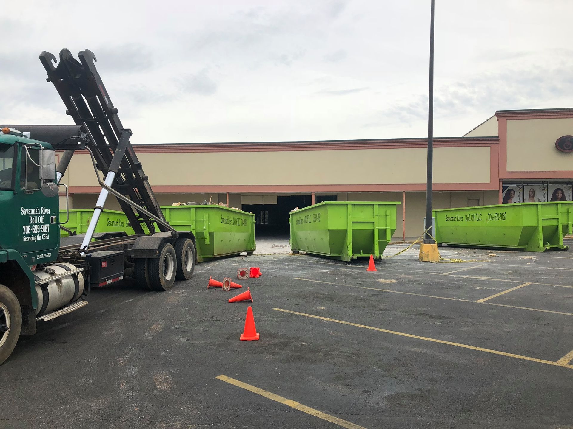 A dumpster truck is parked in a parking lot in front of a building.