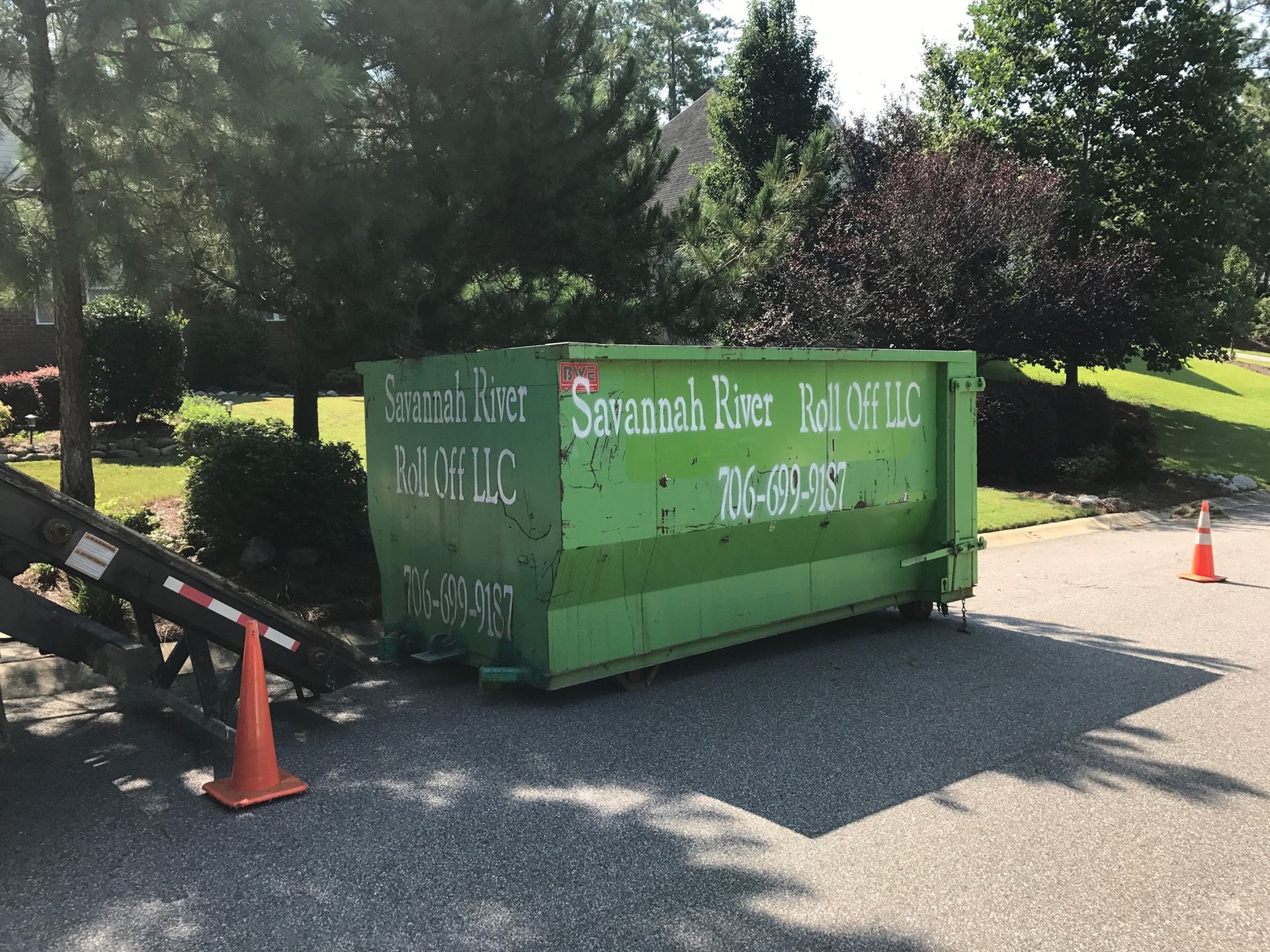 A green dumpster is parked on the side of the road