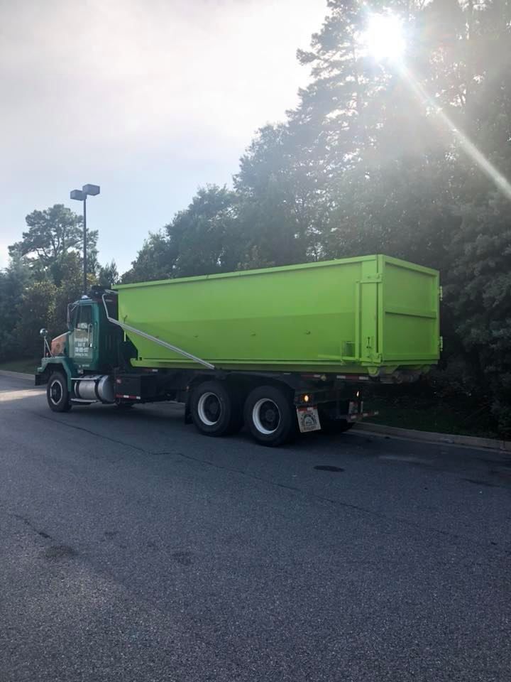 A green dump truck is parked on the side of the road.