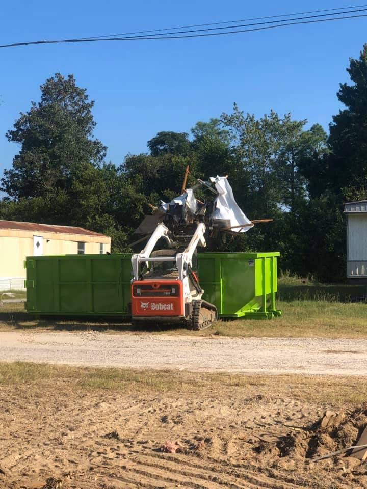 A bobcat is loading junk into a green dumpster.