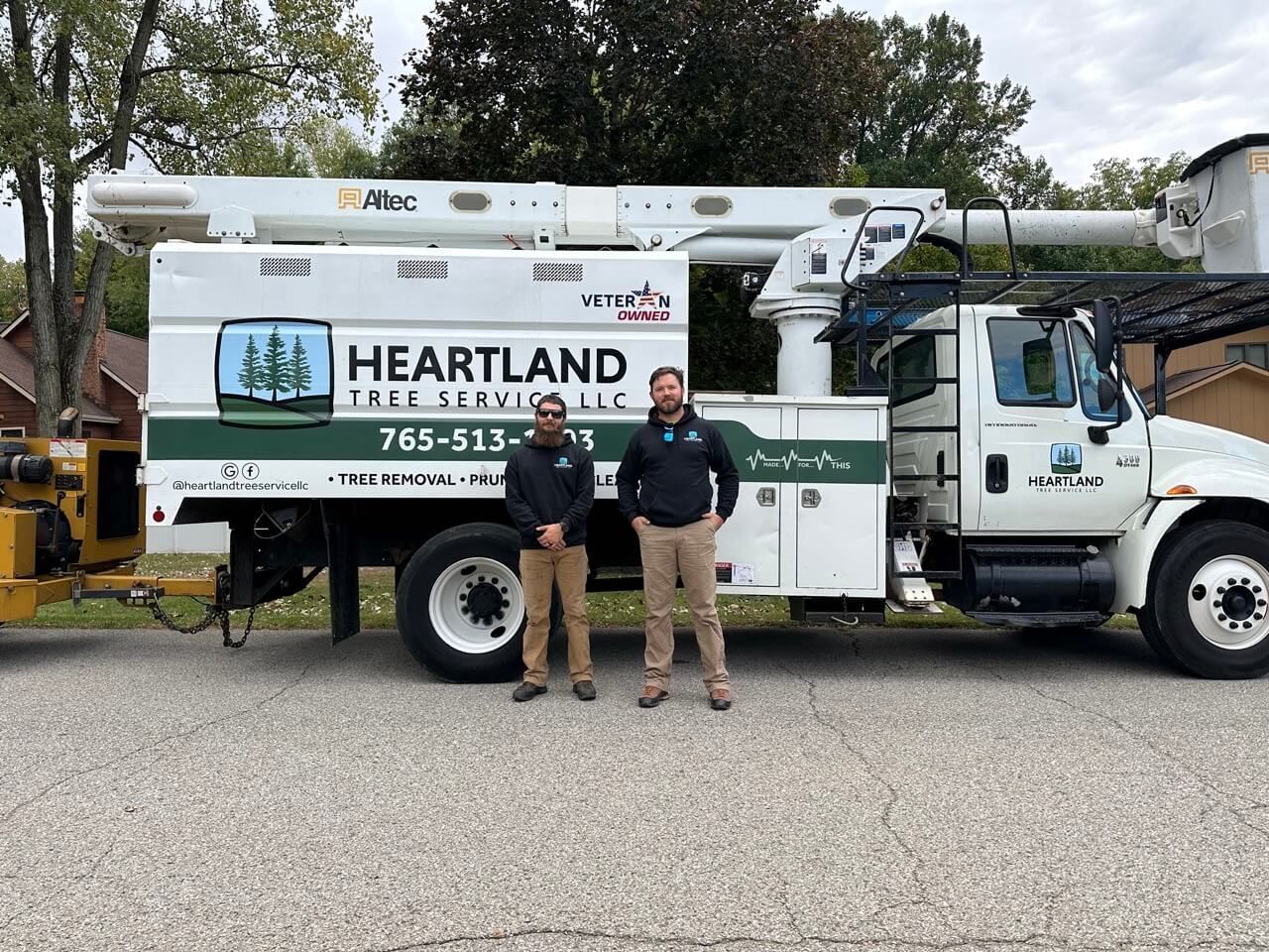 Two men are standing in front of a heartland tree service truck.