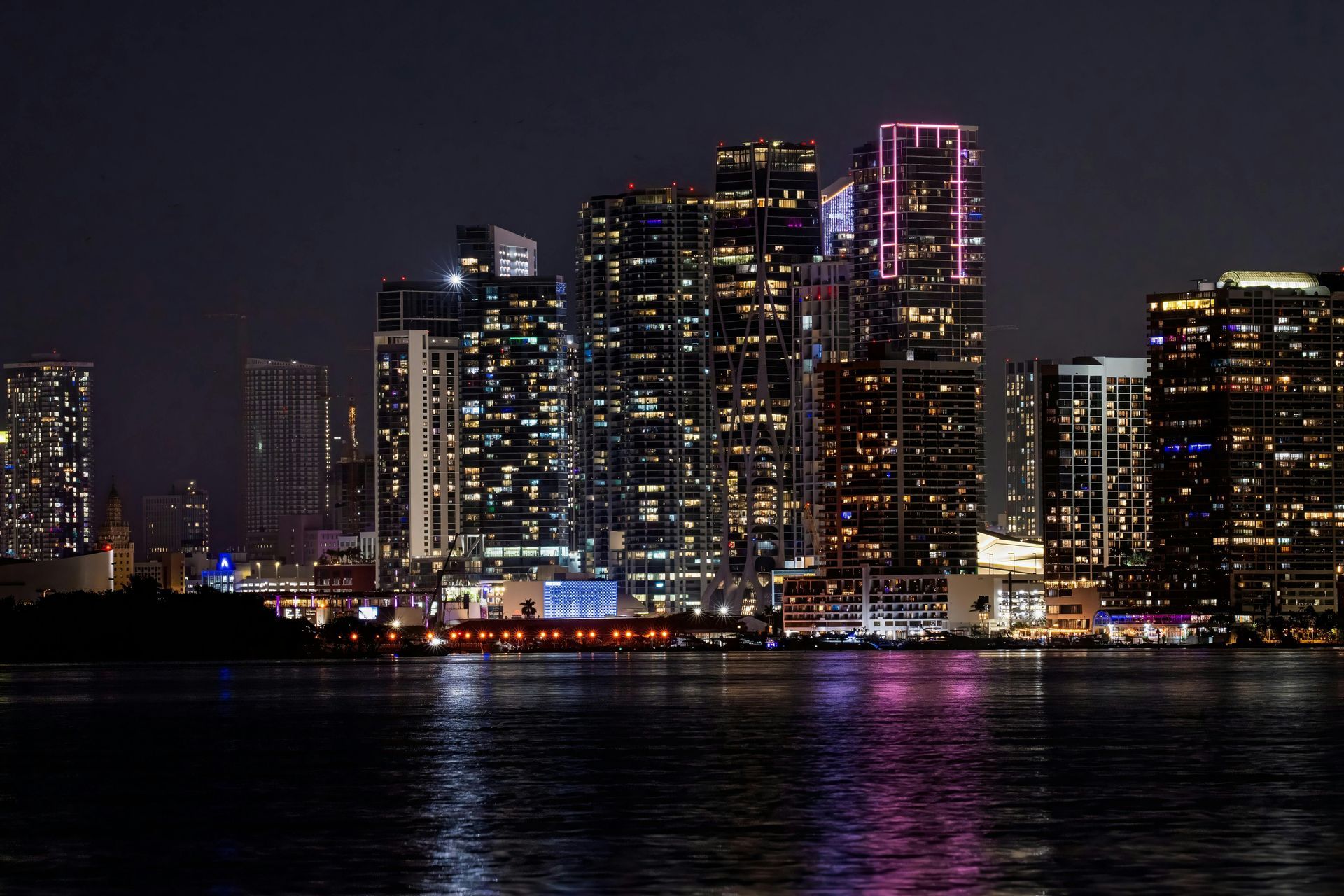City skyline at night with illuminated skyscrapers reflected on dark water.