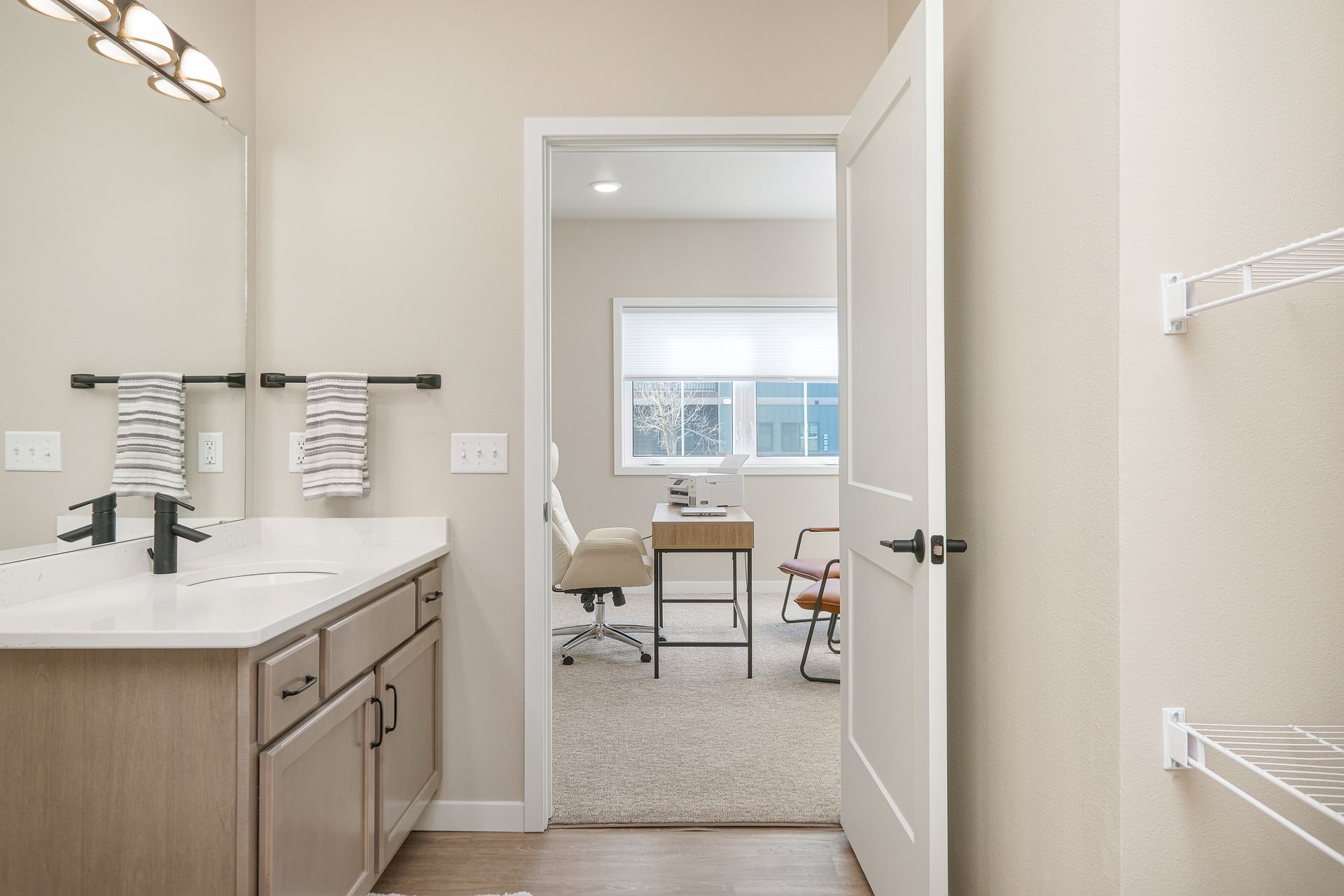 A bathroom with a sink and a mirror and a door leading to a bedroom.