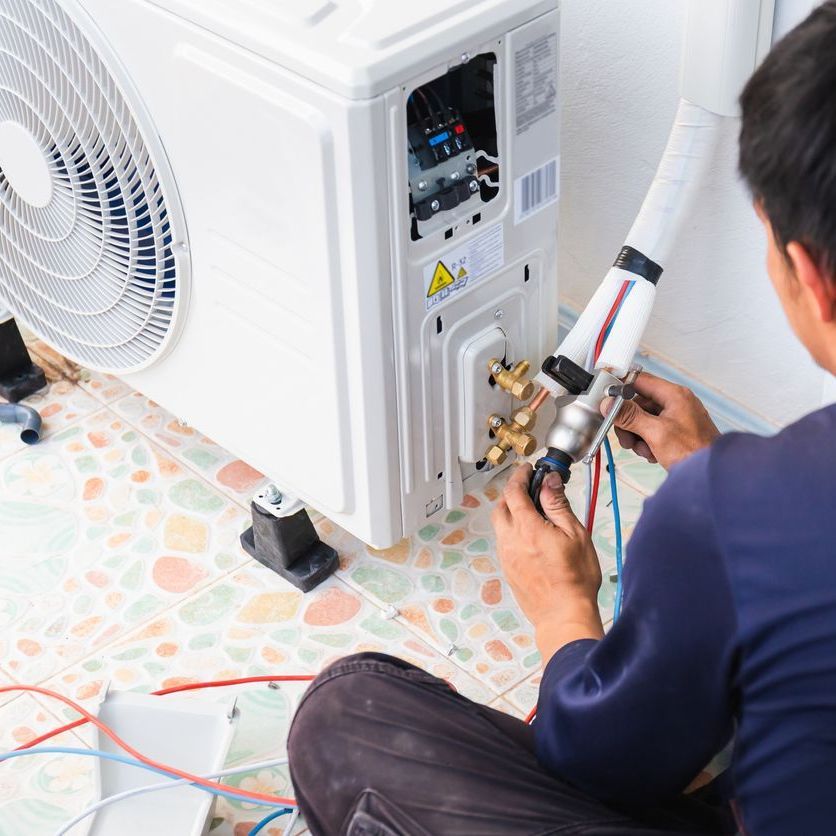 a man is sitting on the floor working on an air conditioner