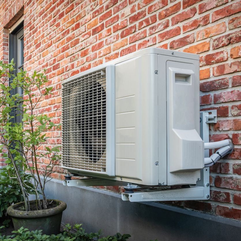 a white air conditioner is mounted on the side of a brick building .