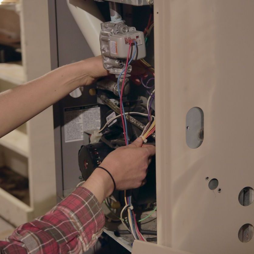 a person in a plaid shirt is working on a heater